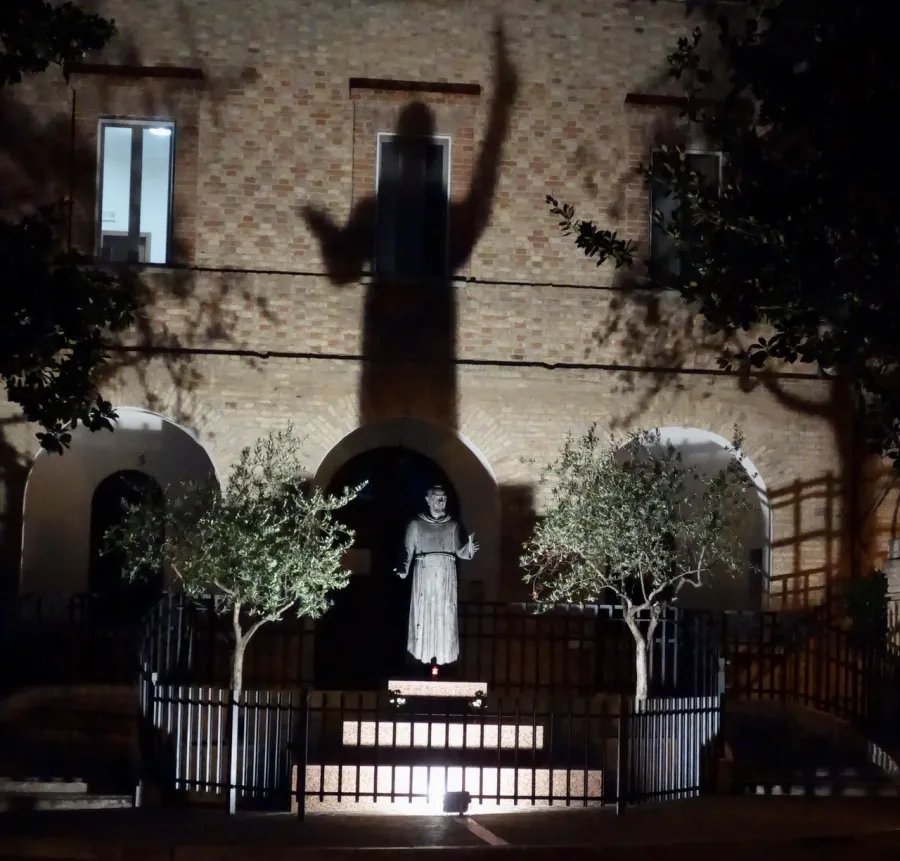 "Die Statue von Pater Pio wird von unten angeleuchtet, sodass sein Schatten mit hoch erhobener Hand wie ein riesiger Schutzschild auf das Konventsgebäude fällt." 