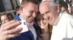 Ein frischvermähltes Ehepaar macht auf dem Petersplatz ein Selfie mit dem Papst.  / L'Osservatore Romano