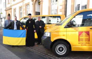 Vikar Ihor Tril (2.v.r.) und Witalij Gamerman (2.v.l., mit Ukraine-Fahne) von der ukrainischen Gemeinde in Paderborn nehmen die beiden BONI-Busse vor dem Bonifatiushaus in Empfang. Rechts im Bild der Generalsekretär des Bonifatiuswerkes, Monsignore Georg Austen, links Geschäftsführer Ingo Imenkämper.  / Bonifatiuswerk/Oliver Gierens