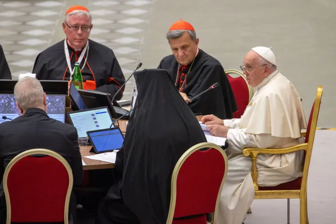 Jesuitenkardinal Jean-Claude Hollerich (links) blickt auf seinen Ordensbruder, Papst Franziskus bei der Synodalitätssynode im Vatikan, Oktober 2023. Zwischen den beiden sitzt Kardinal Mario Grech.