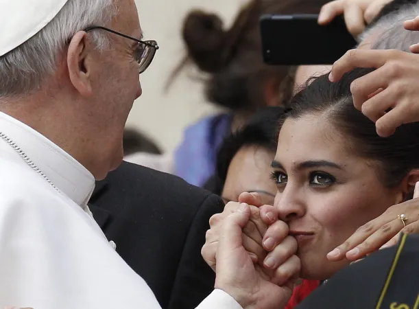 Eine junge Frau küsst die Hand von Papst Franziskus.