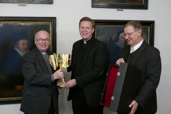 Dompropst Gerd Bachner (v.l.), Generalvikar Dr. Dominik Meiering und Dr. Rudolf Solzbacher, Direktor der Diözesanstelle Weltkirche/Welt-mission, begutachten die Reliquie und ihre Vorbereitung für die Reise.